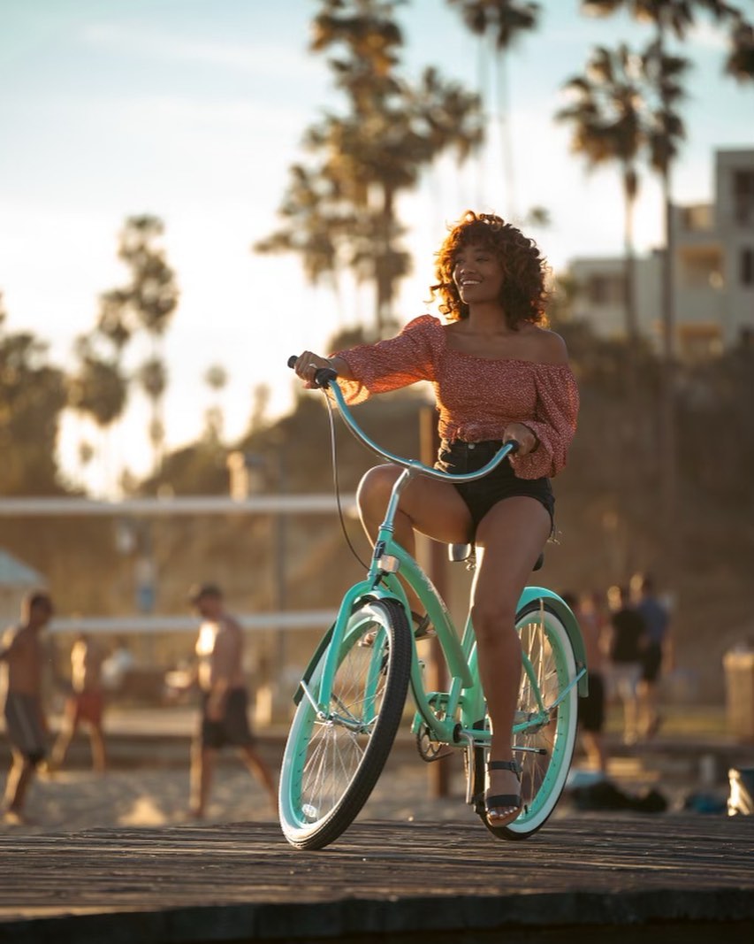 Woman riding a mint green bella bike on a wooden platform with palm trees in the background